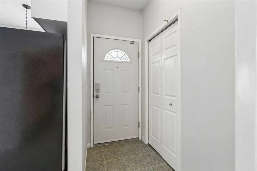 Entryway with a white door, a small window on the door, a gray refrigerator on the left, and closet doors on the right, with beige tile flooring.