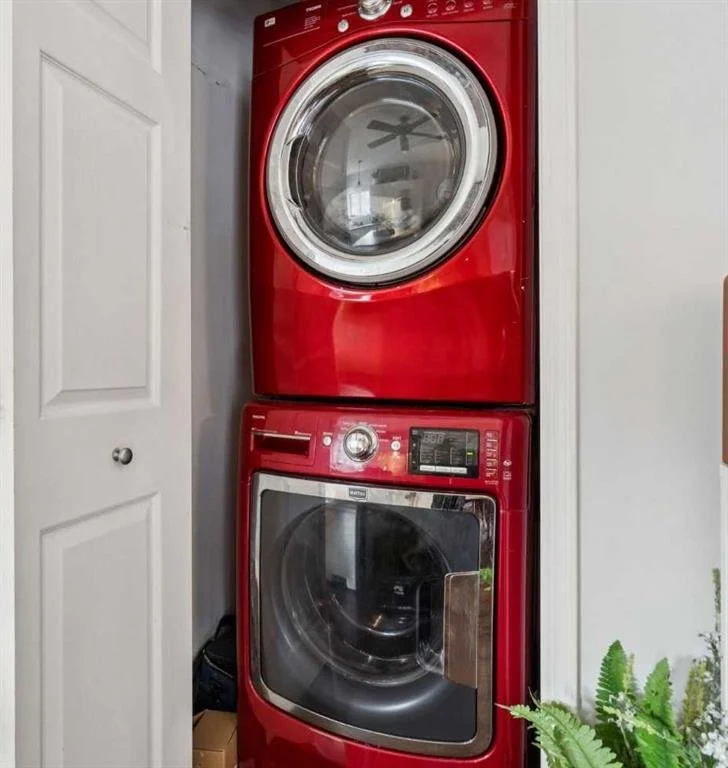 Red stacked washer and dryer in a laundry area with a white door on the left and green plants on the right.