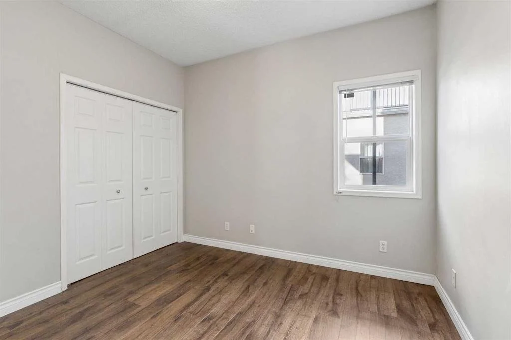 Empty bedroom with white walls, a wood floor, a window, and a closet with two white doors.