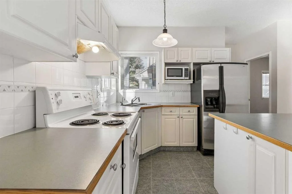 White kitchen with countertops, cabinets, a refrigerator, microwave, stove, and window.