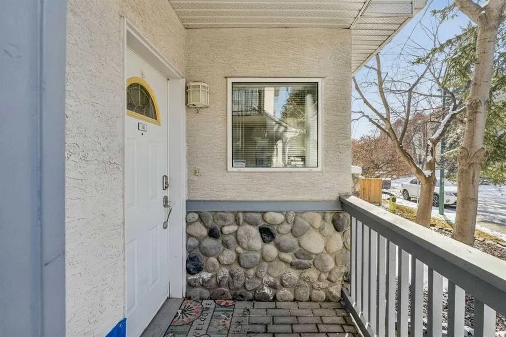 Front porch area with white door, window, stone foundation, and wooden railing, with trees and street visible outside.