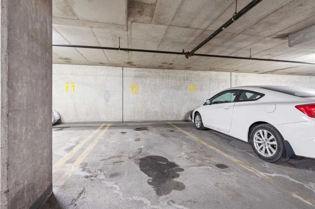 Underground parking garage with numbered parking spots and two parked cars, one white and one silver.