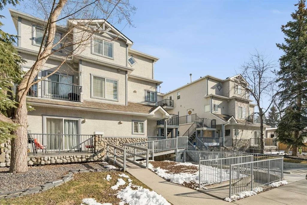 Multi-story residential apartment complex with balconies, stairs, and outdoor walkways, surrounded by trees with some snow on the ground.