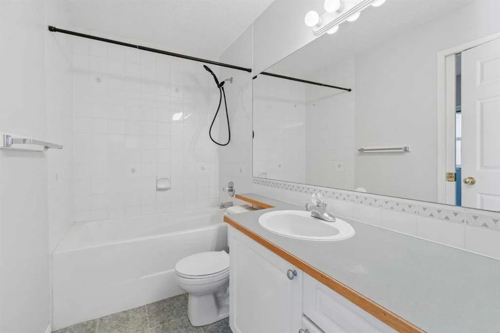 Bathroom with bathtub, toilet, sink, large mirror, and white tiles.