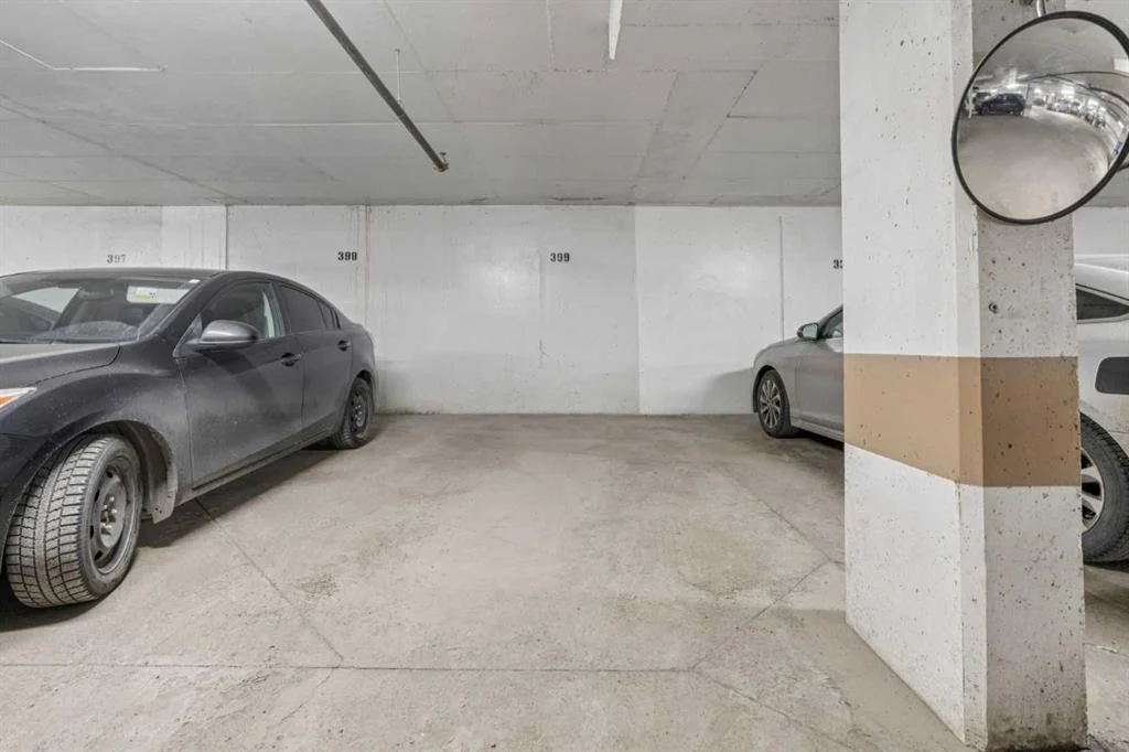 Underground parking garage with three parked cars and a wall with parking spot numbers. Mirror reflecting the parking lot.