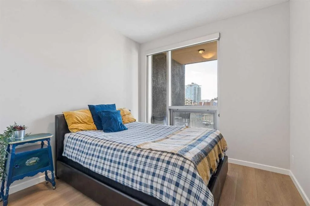 Bedroom with a bed, blue nightstand, and a large window with city view.