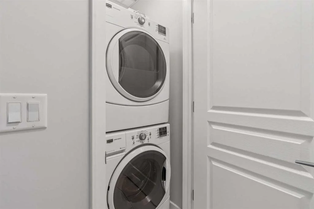 Stacked white front-loading washer and dryer in a laundry closet with white walls and door.