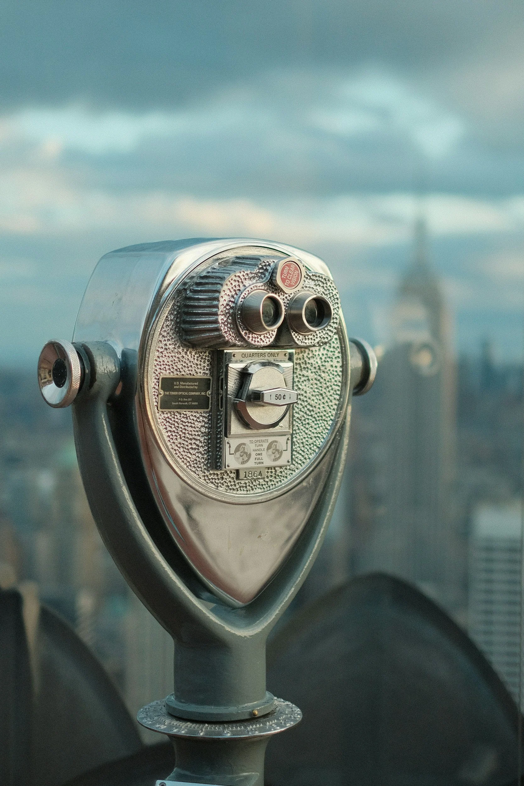 A coin-operated binocular viewer on a city balcony, with a view of the city skyline and the Eiffel Tower in the background.