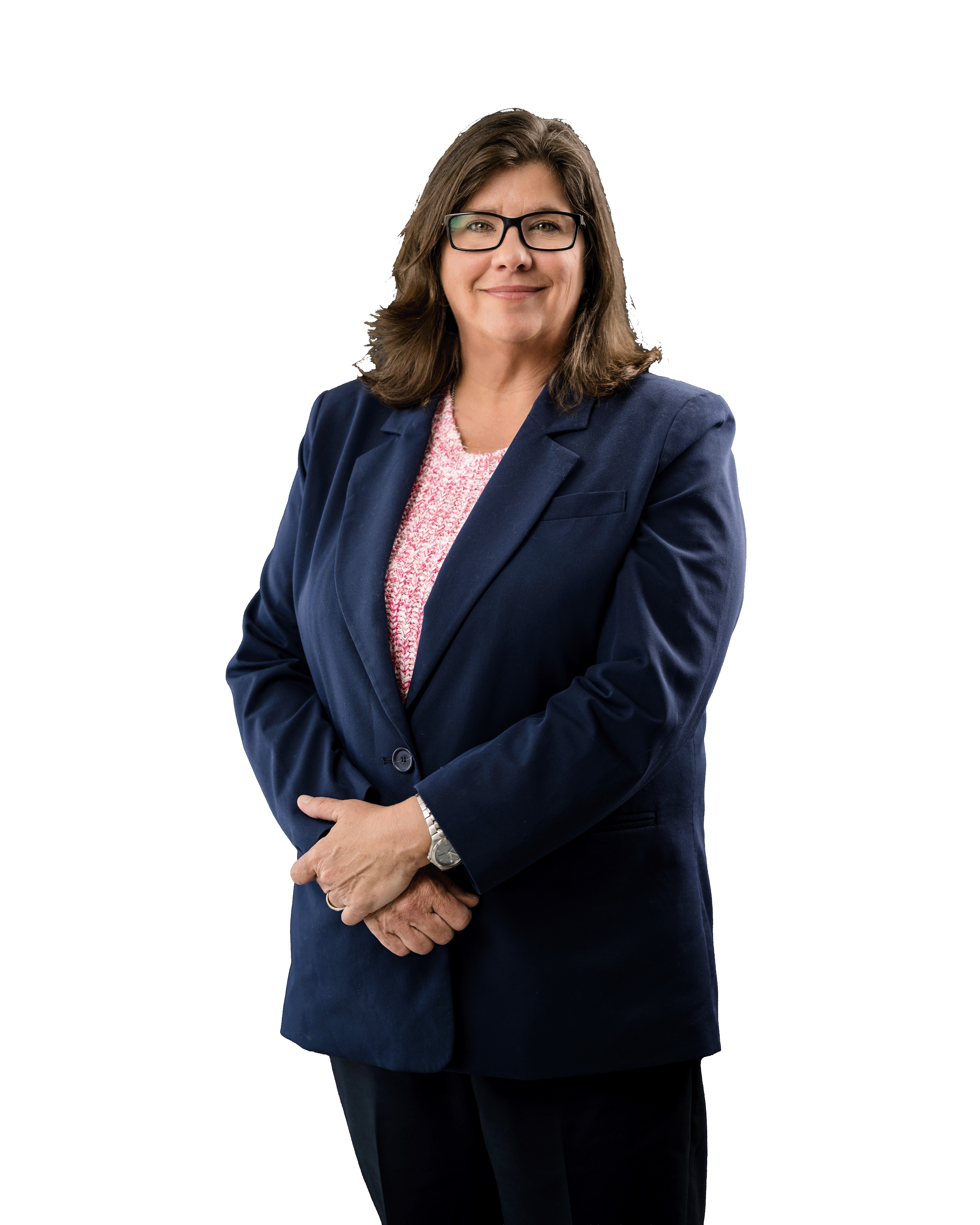 A woman with shoulder-length brown hair, glasses, and a slight smile, wearing a navy blazer, pink patterned blouse, black pants, and a silver watch, standing against a white and black background.