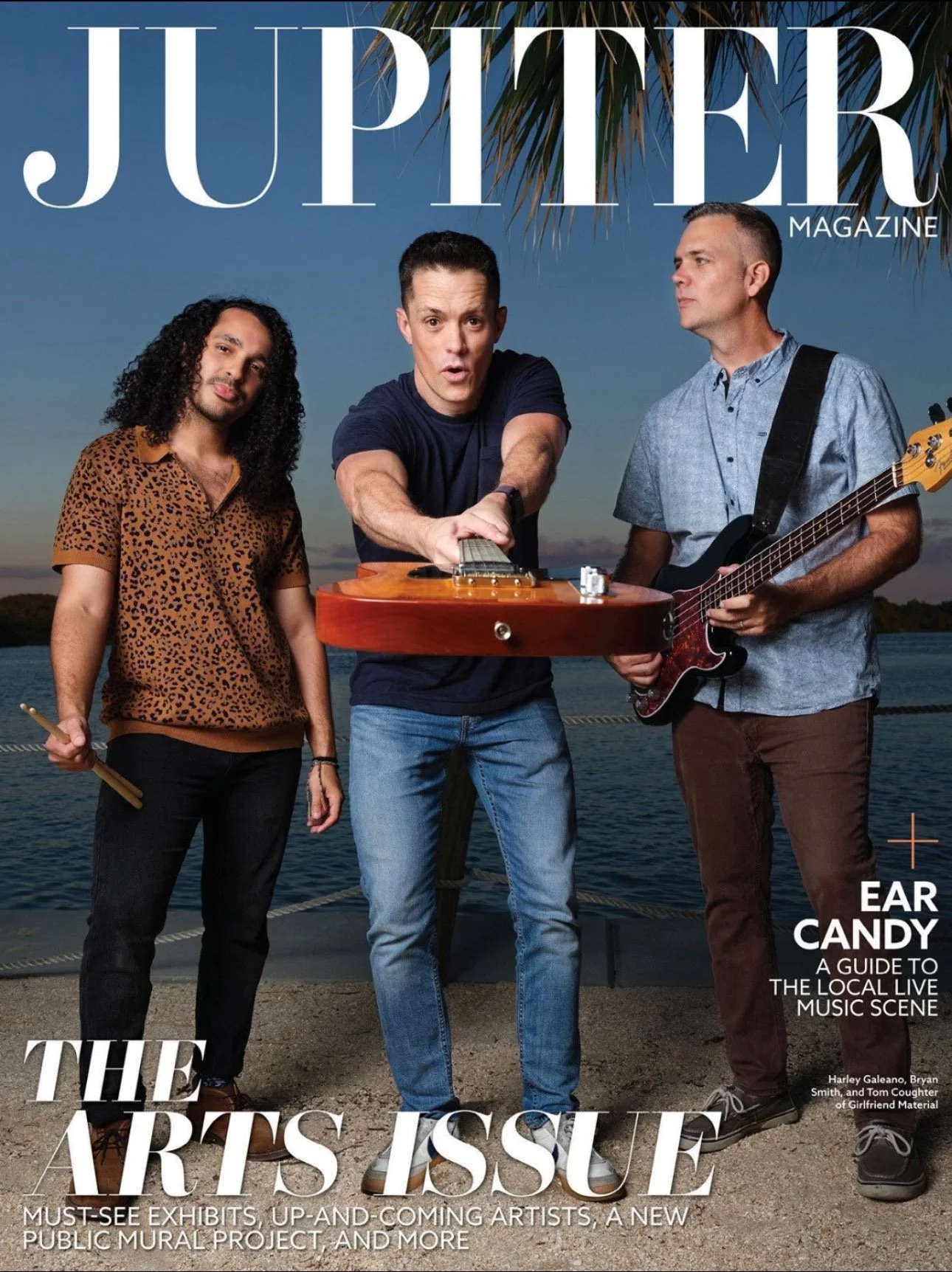 Cover of Jupiter Magazine featuring three men by a body of water at sunset. One holds a drumstick, another is playing a guitar, and the third is adjusting a guitar. The title reads 'The Arts Issue' with subheadings about local live music and artists.