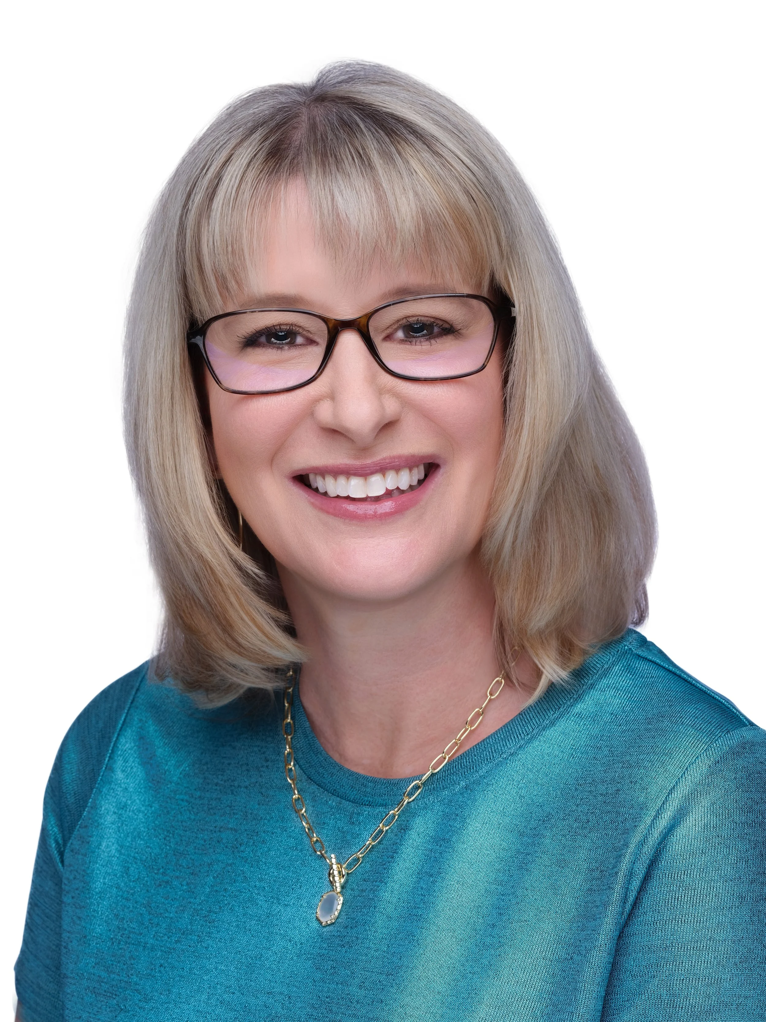 A woman with blonde hair and glasses smiling, wearing a teal shirt and a gold necklace with a pendant.