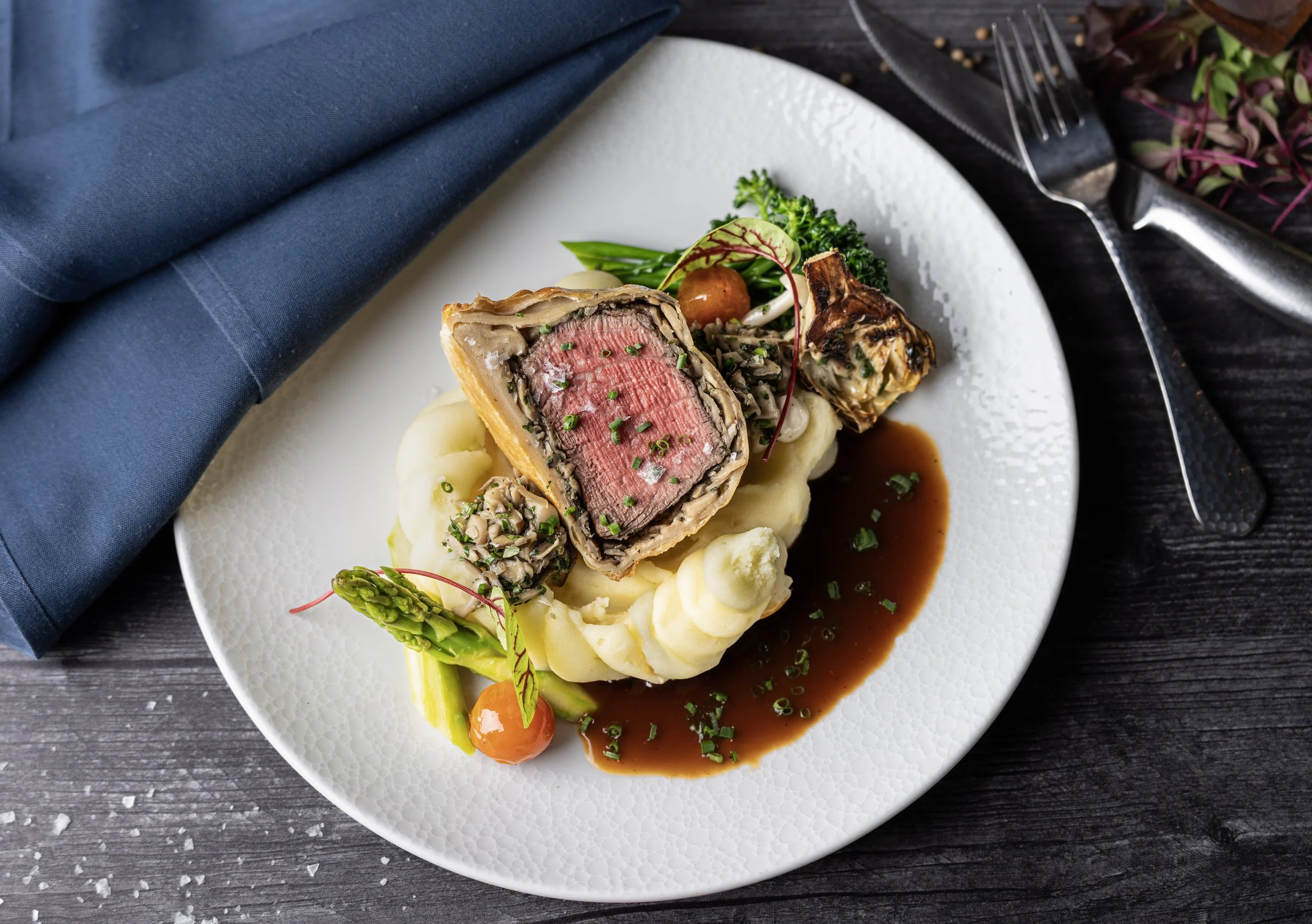 Restaurant food photography featuring a plated beef entrée with mashed potatoes, vegetables, and sauce.