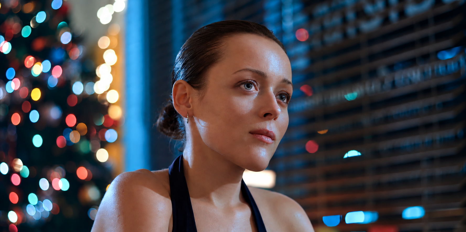A young woman with slicked-back hair and hoop earrings looks thoughtfully to her right, with colorful bokeh lights and a blue wall in the background.