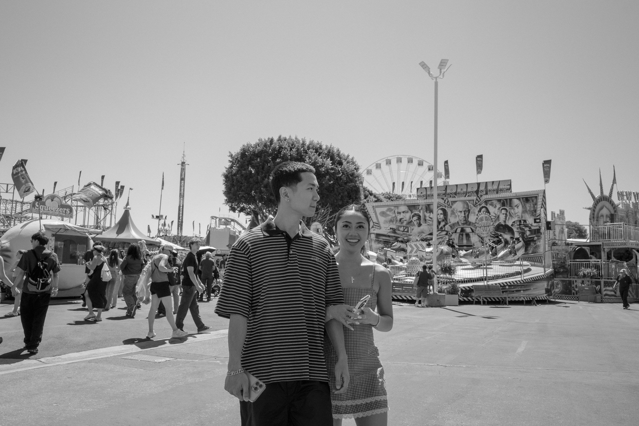 Two teenagers, a boy and a girl, standing in front of a carnival with rides and crowds.