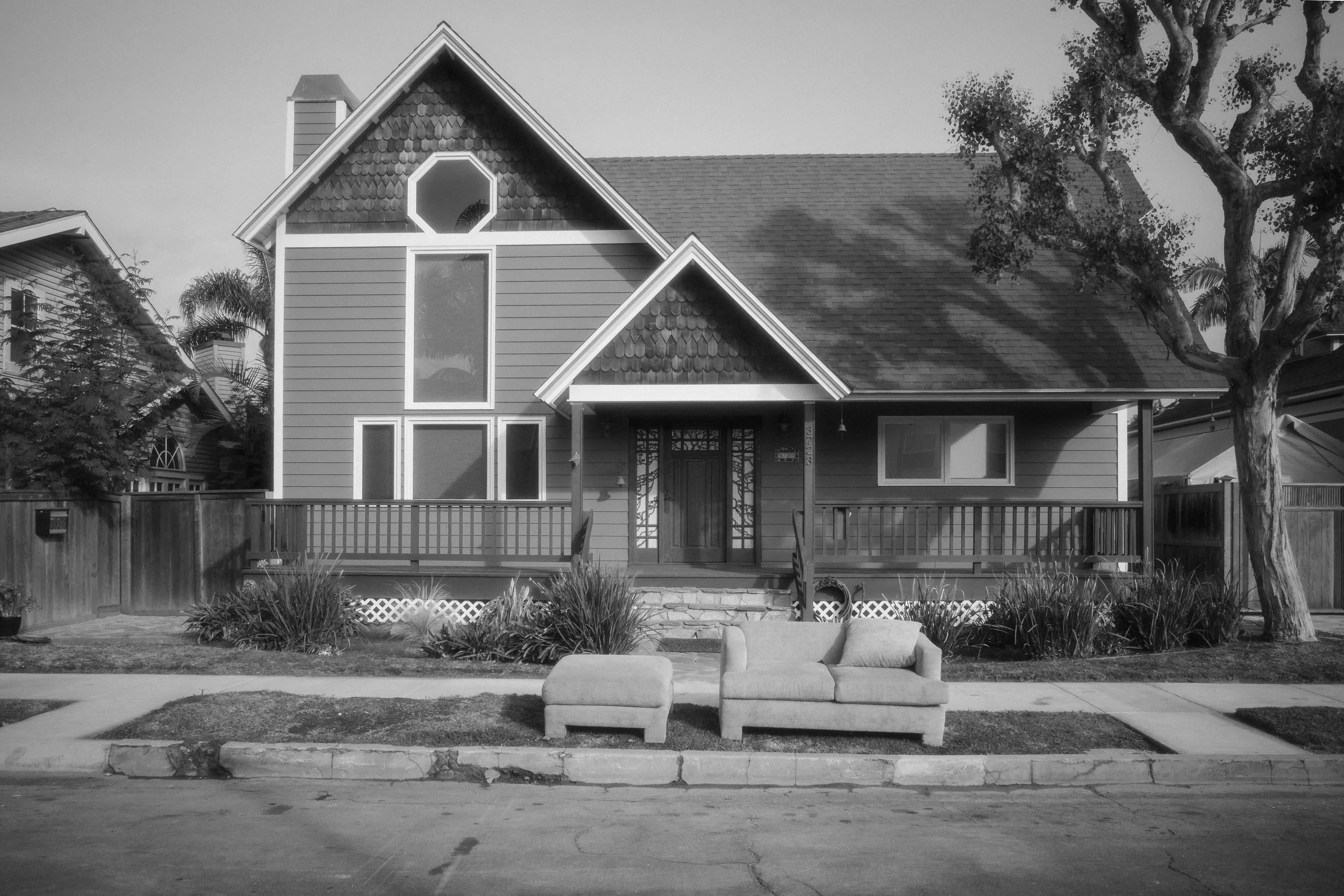 A two-story house with a front porch, a large window, and a sofa on the sidewalk in front of it.