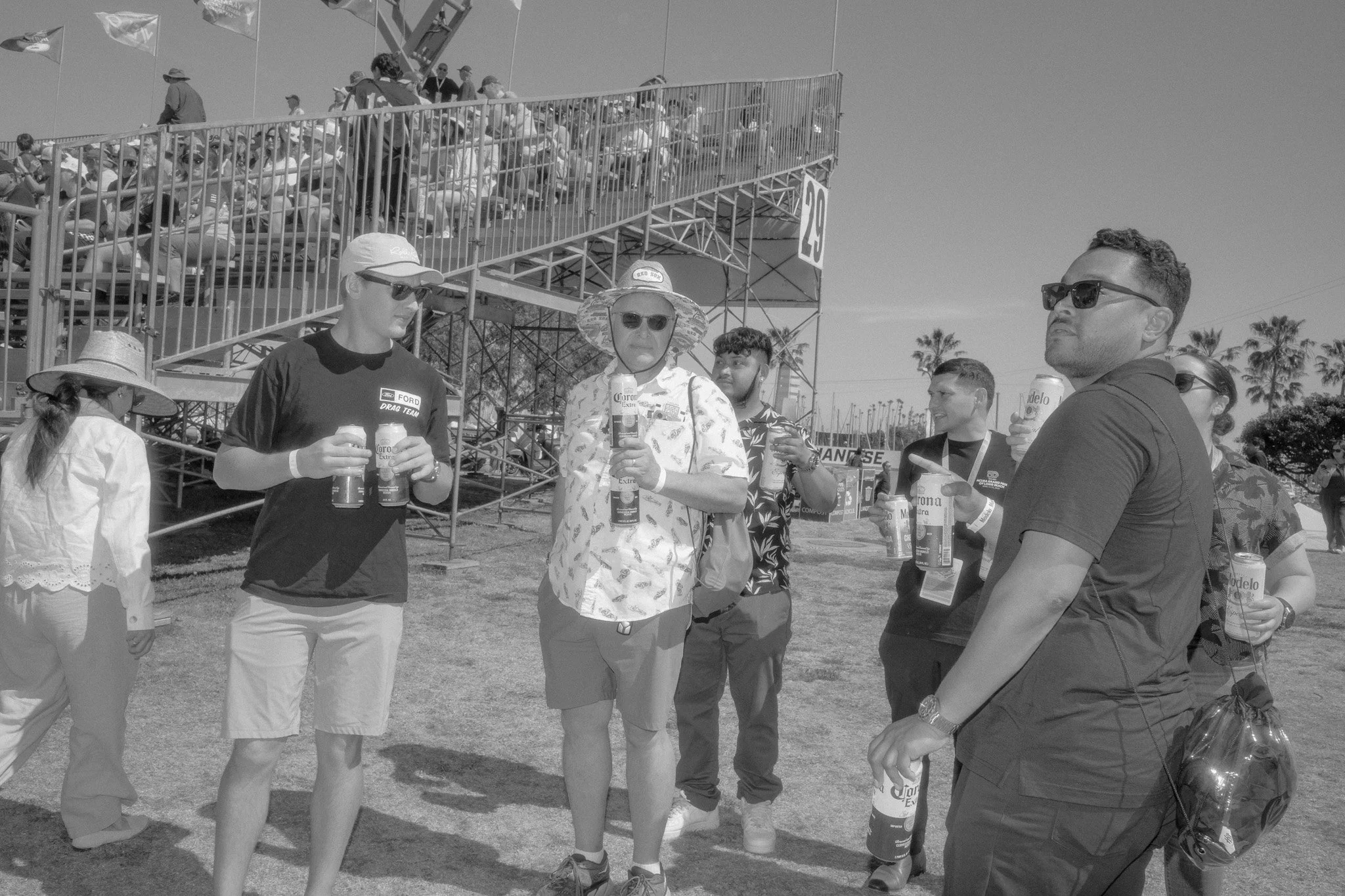 People standing outdoors at a festival or event, holding drinks, with a staircase and tents in the background.
