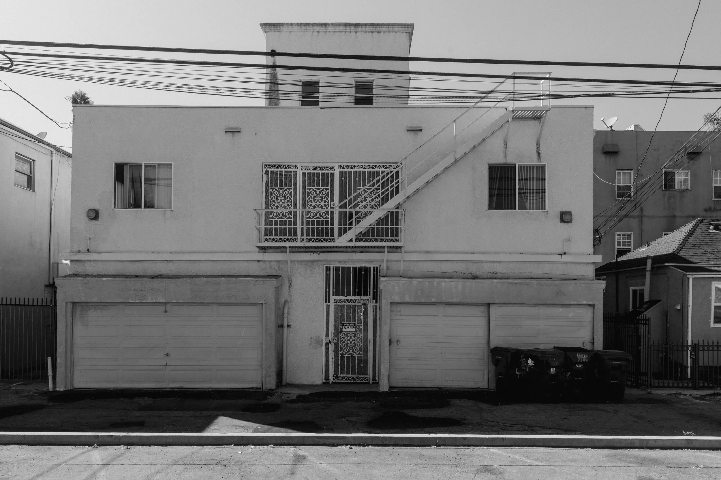 Black and white photo of a two-story building with two garage doors and an external staircase, with power lines overhead.