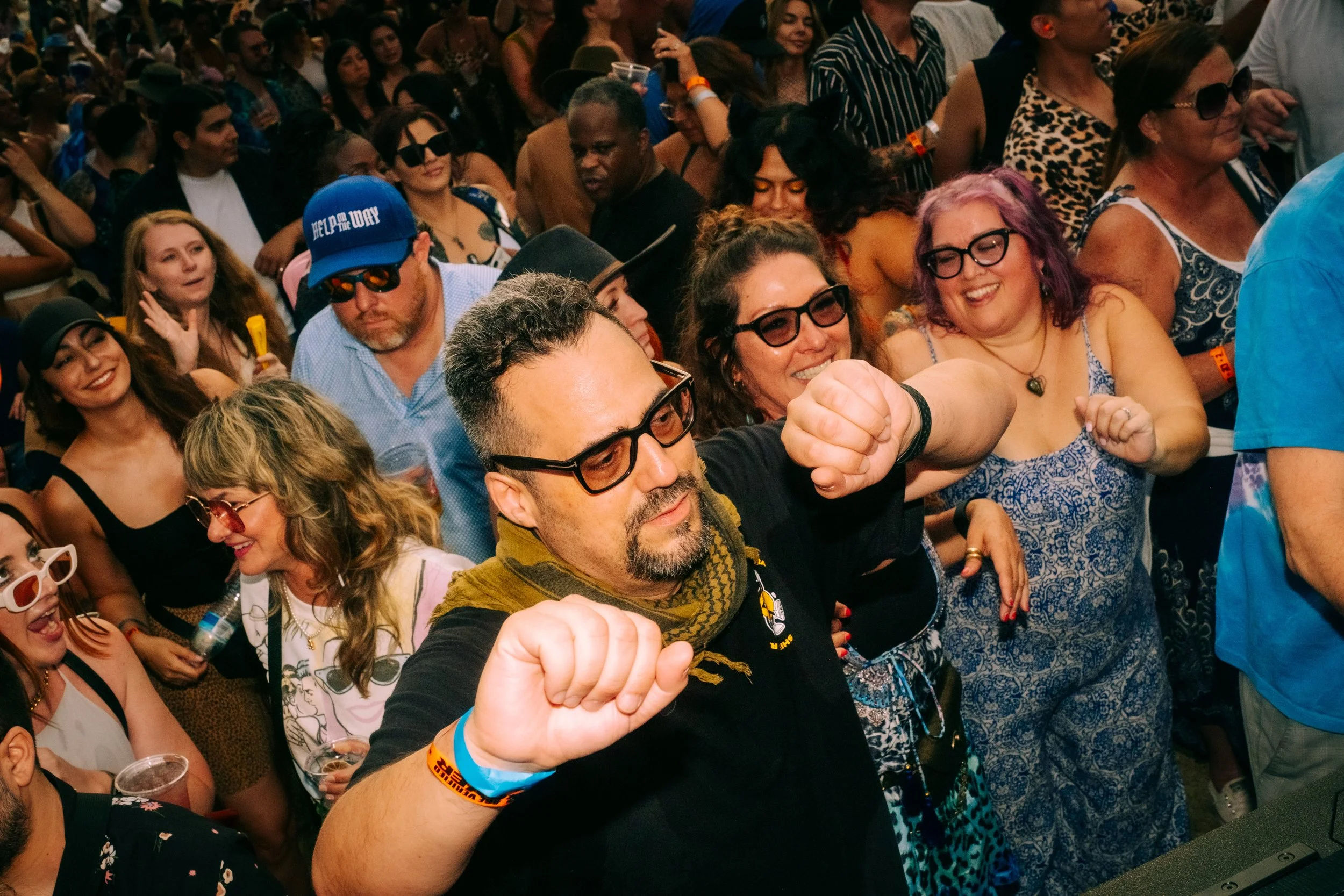 A man with glasses at a concert or party, dancing with friends in a crowd, surrounded by smiling and enjoying people.