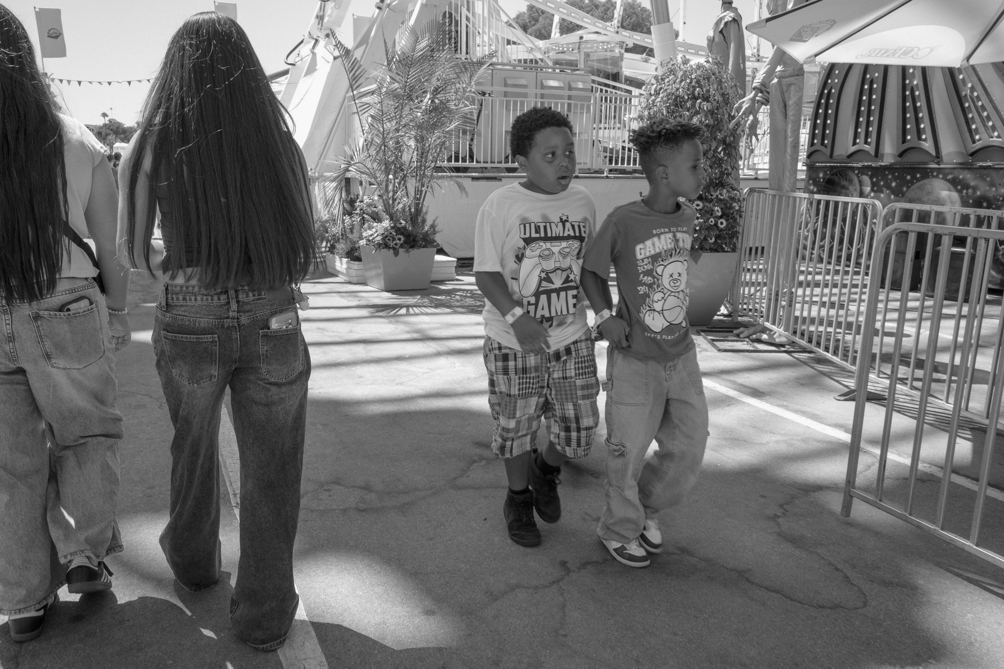 Two boys walking hand in hand at a carnival with amusement rides and tickets booths in the background.