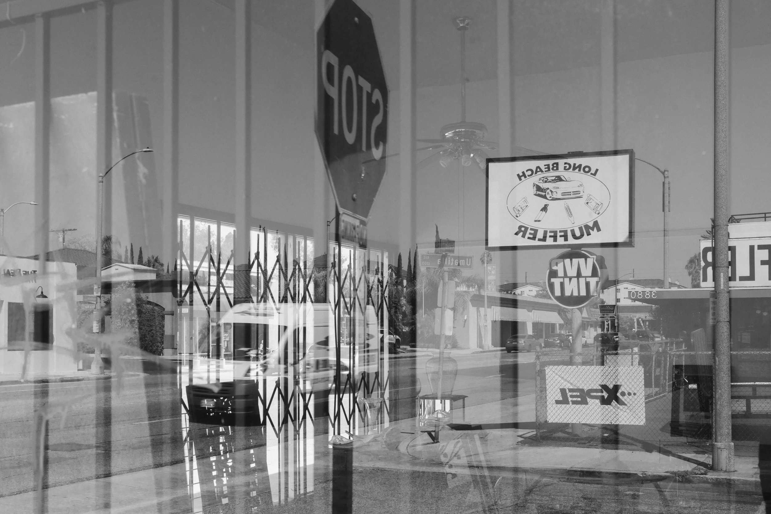 Reflection of a street scene with stop sign, business signs, and buildings seen through a glass window with a security gate.