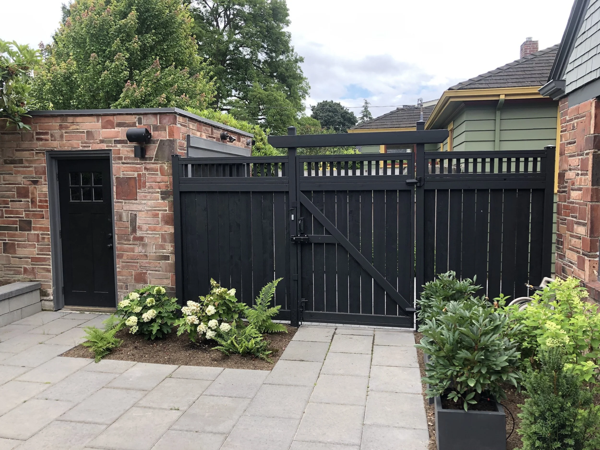 Backyard patio with black wood fence gate, brick garage, and stone pavers — Magnolia, Seattle full home remodel