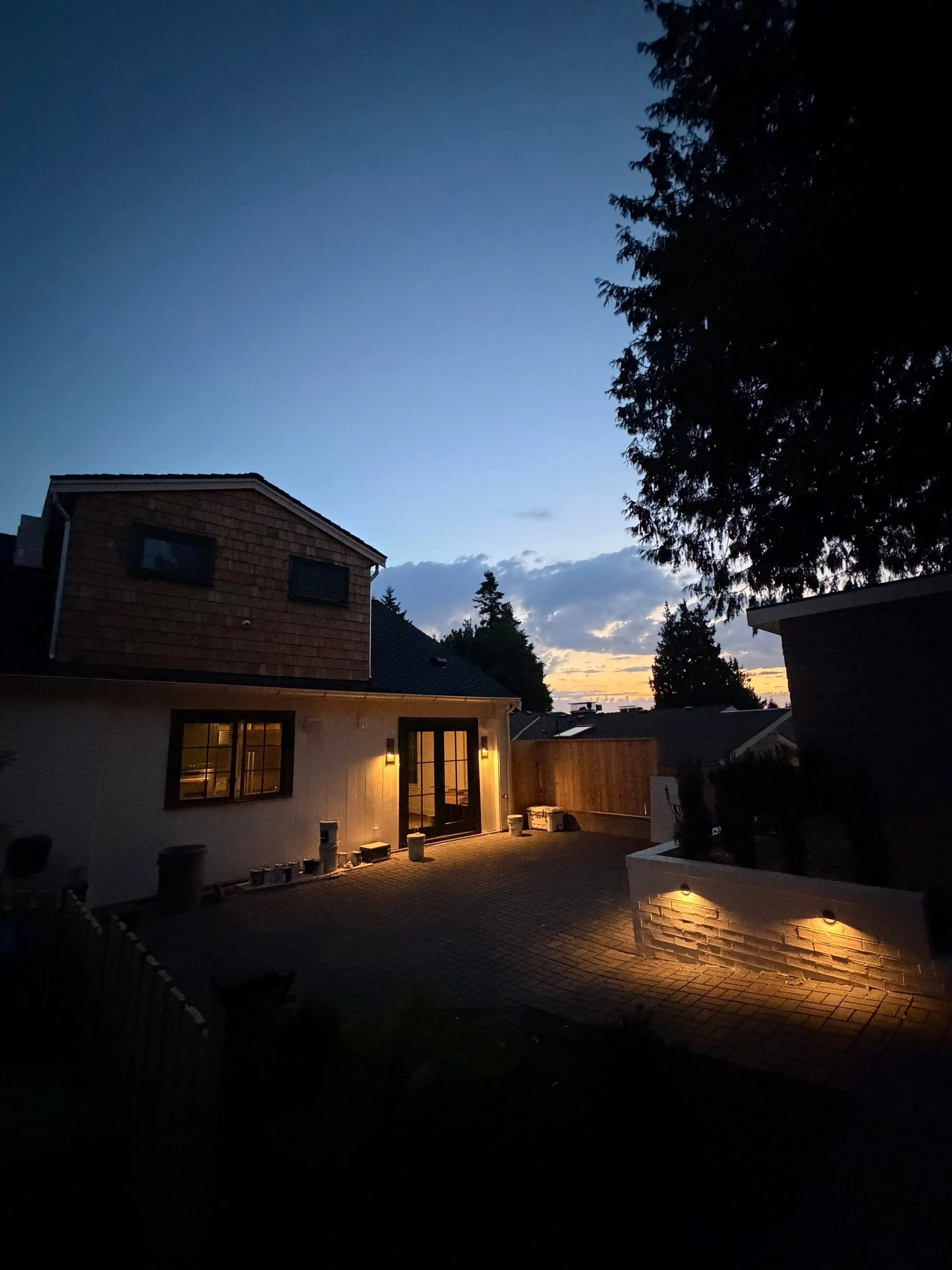 Evening view of the backyard addition with outdoor lighting and mature trees — Discovery Park, Seattle whole-home addition