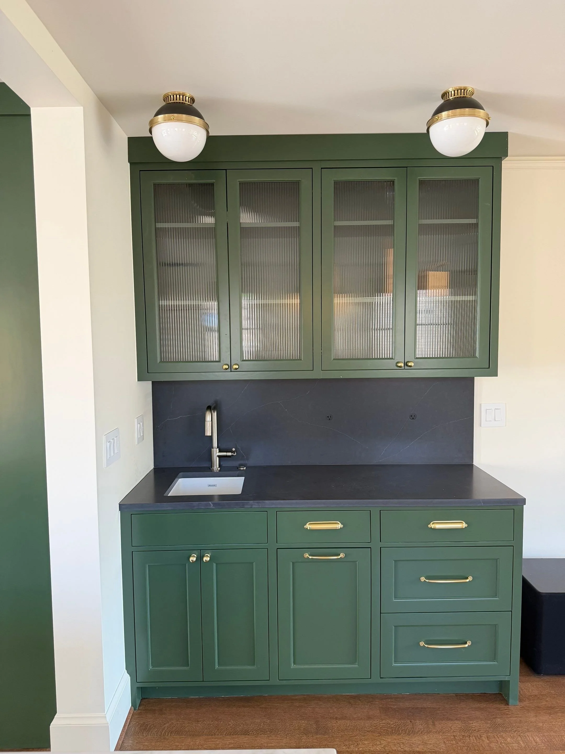 Built-in bar cabinet with glass-front upper cabinets, black countertop, and brass hardware — Discovery Park, Seattle whole-home addition