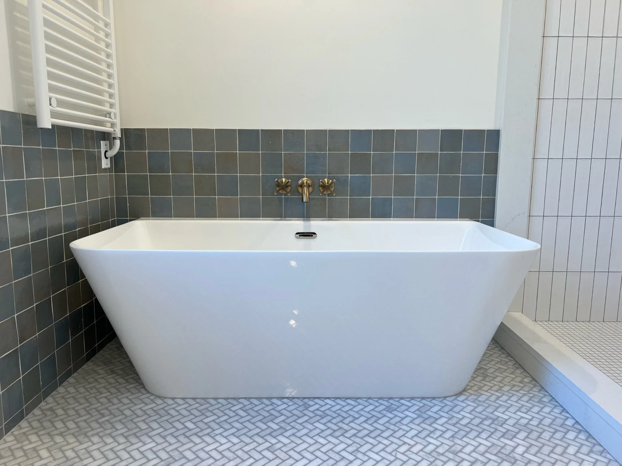 Freestanding soaking tub with wall-mounted filler faucet, blue subway tile, and geometric floor tile — Viewmont, Seattle primary bath remodel