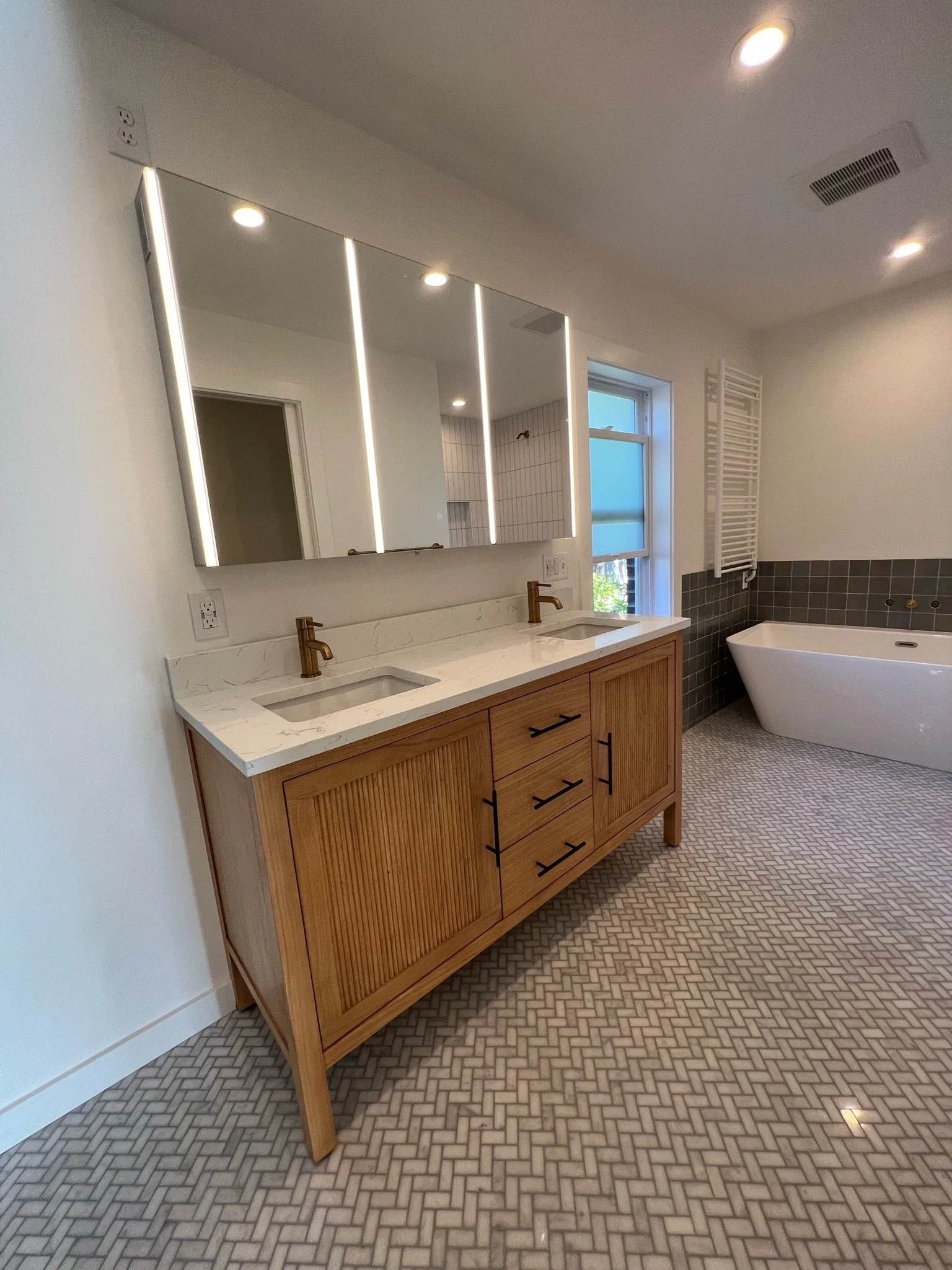 Primary bathroom with double vanity, backlit mirrors, wood cabinetry, and freestanding soaking tub — Viewmont, Seattle primary bath remodel