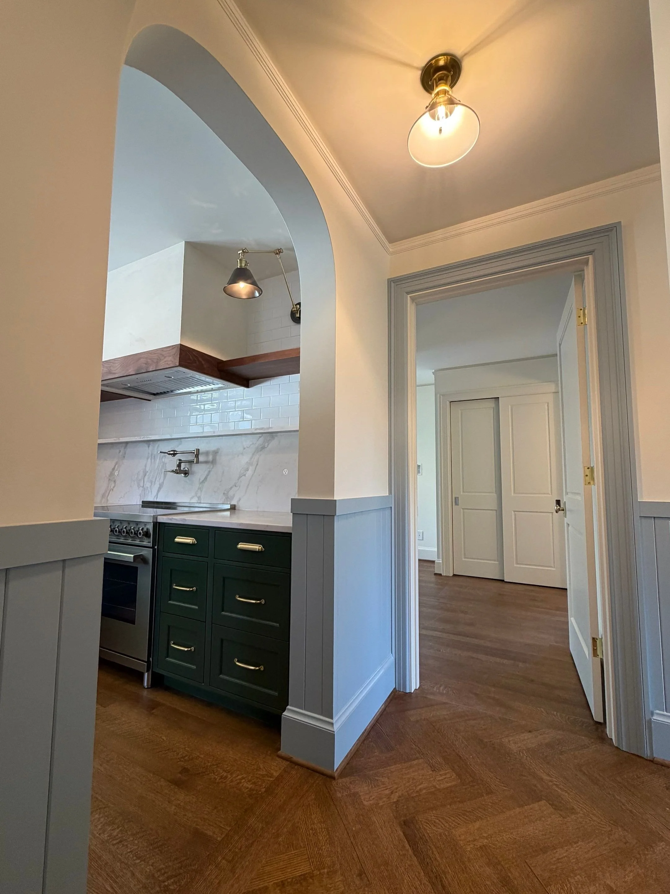 View through an archway into the kitchen with dark green cabinetry and parquet flooring — Discovery Park, Seattle whole-home addition