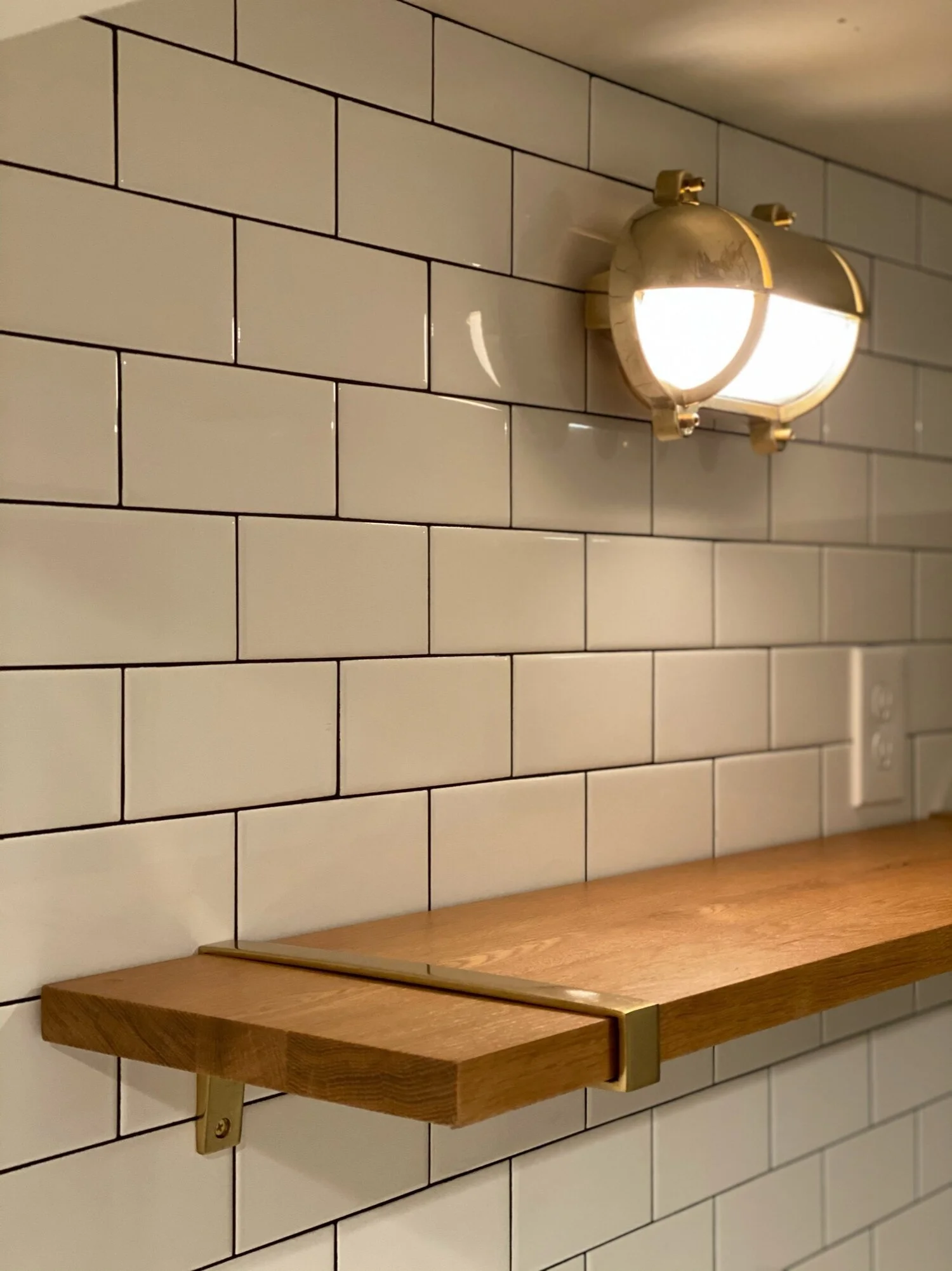 Detail of subway tile wall with wood floating shelf and brass sconce light — Magnolia, Seattle full home remodel