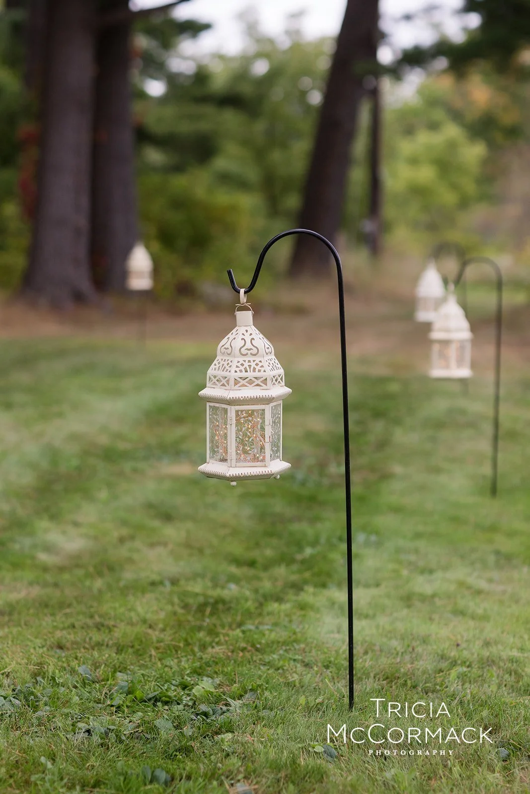White bohemian lanterns hanging on shepherd's crooks to create a wedding ceremony path by Berkshire Event Lighting.