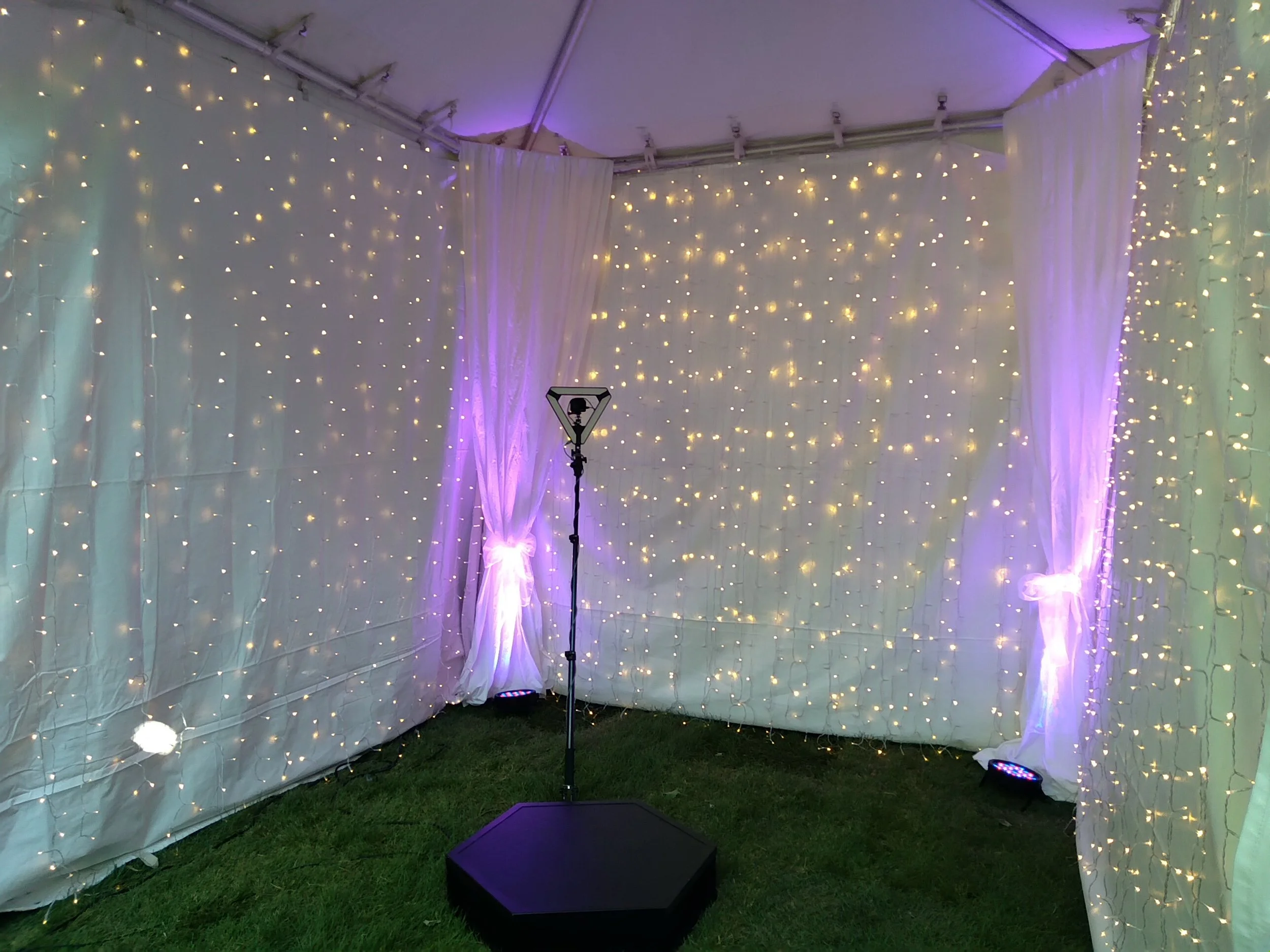 Photobooth tent featuring waterfall curtain lights and corner fabric draping with pink uplighting by Berkshire Event Lighting.