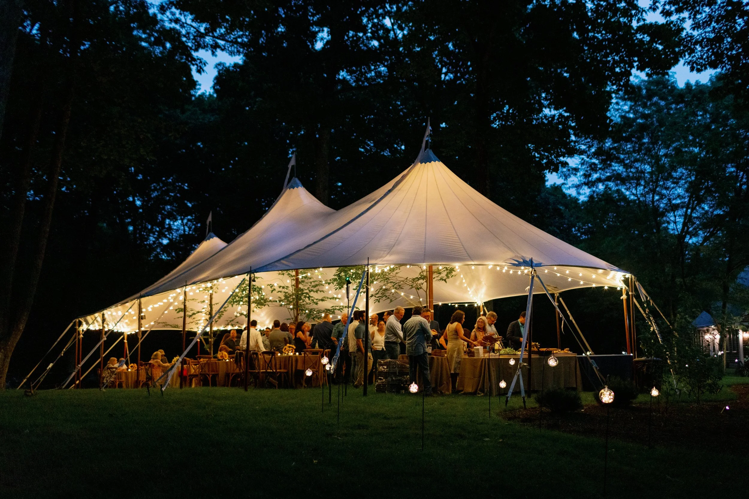 Exterior night view of a glowing sailcloth wedding tent with bistro lighting by Berkshire Event Lighting in Southfield, MA.