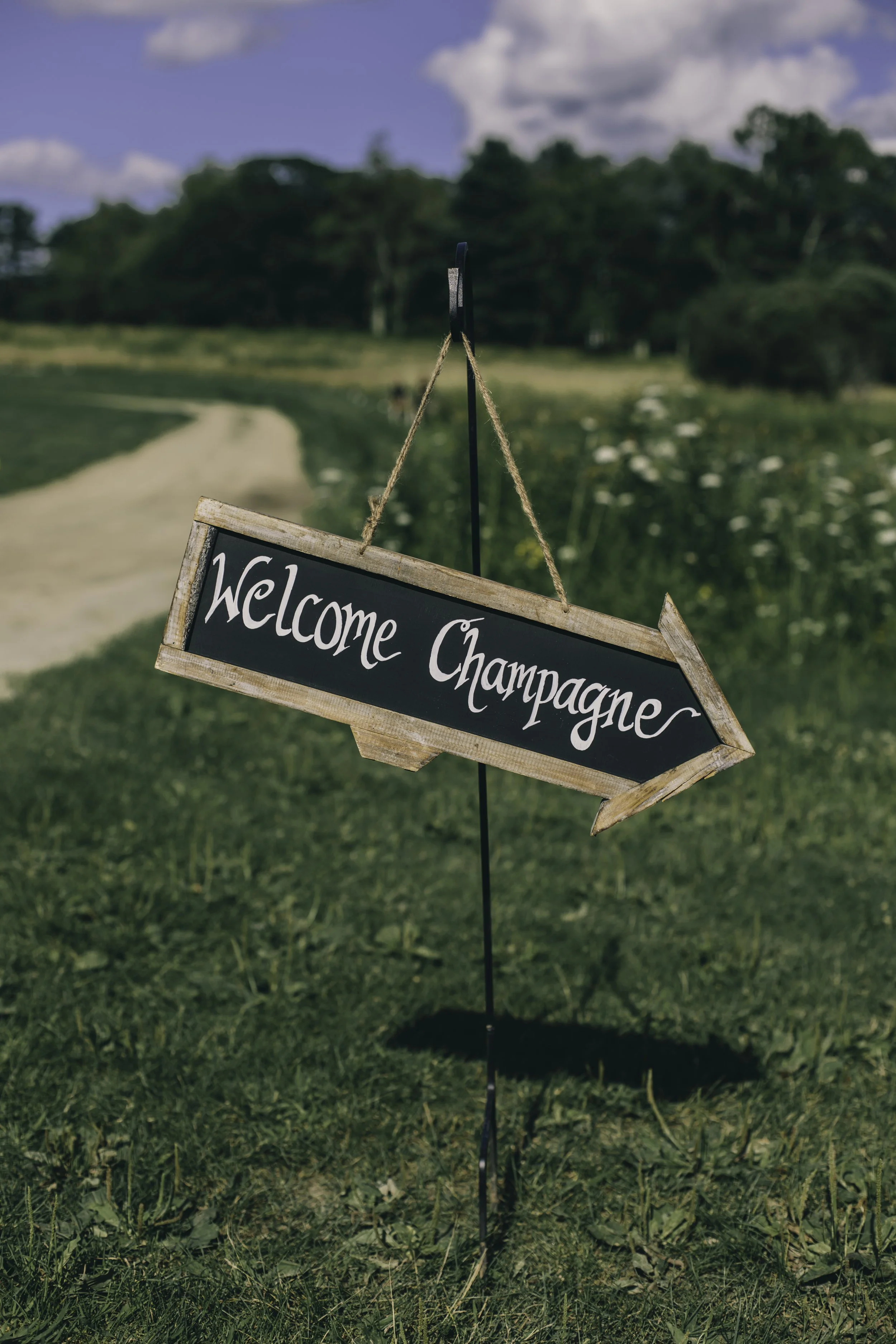 Customizable chalkboard arrow sign hanging on a black shepherd hook for wedding guest wayfinding by Berkshire Event Lighting.