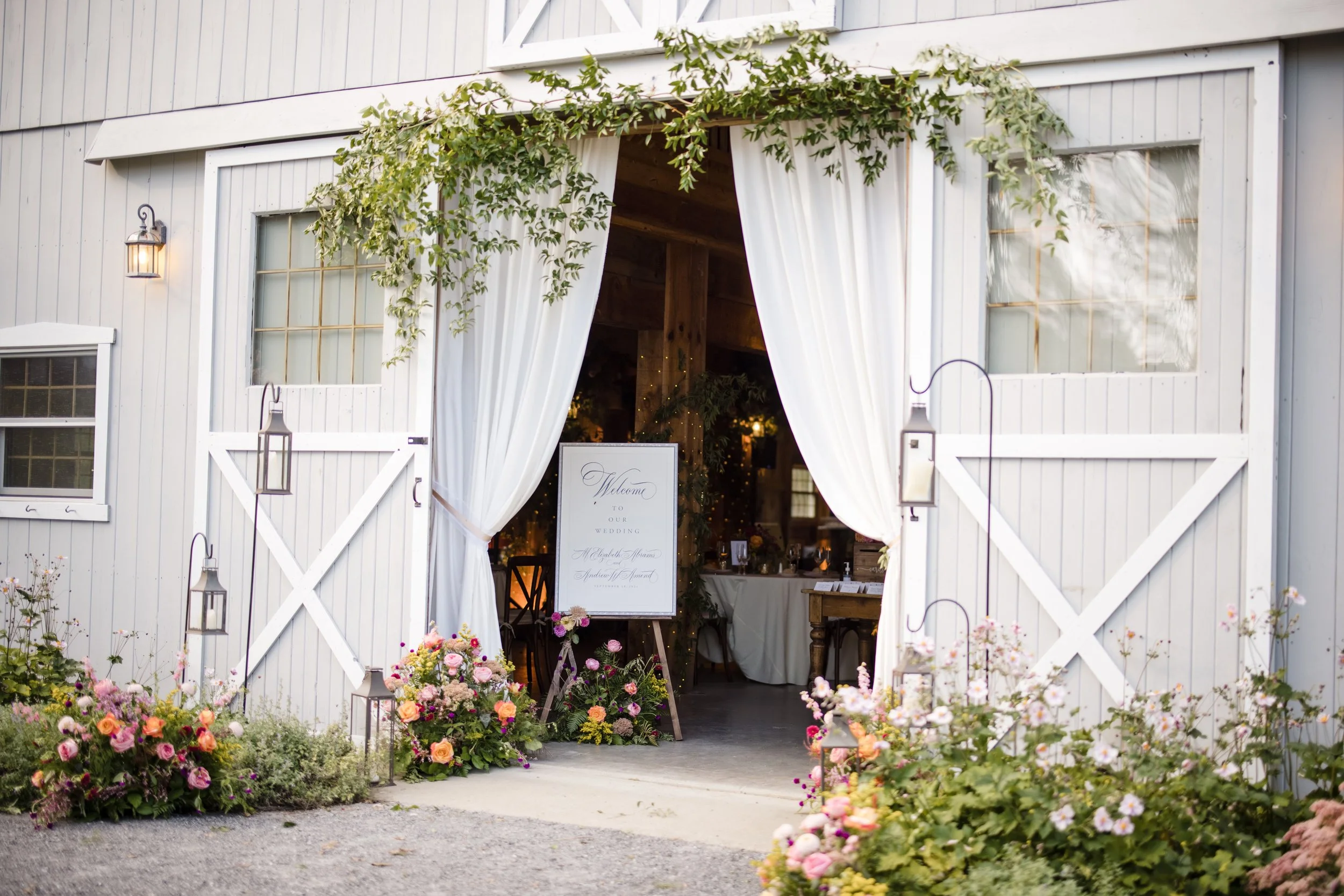 fabric draping framing a rustic barn entrance with clusters of metal lanterns on shepherd crooks in Huudson NY. by Berkshire Event Lighting