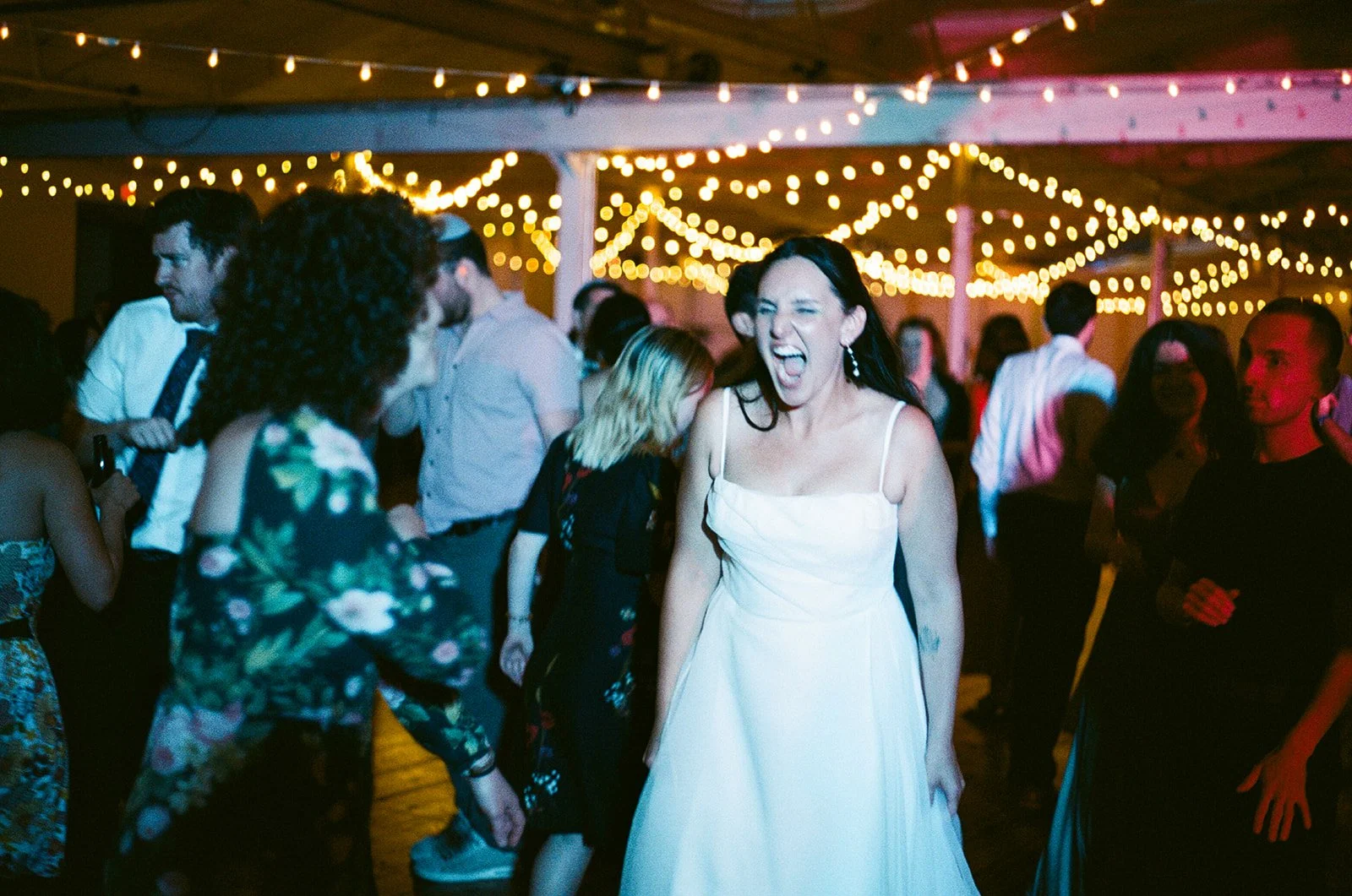 Happy bride dancing under a massive bistro light installation by Berkshire Event Lighting at Greylock WORKS, North Adams MA.