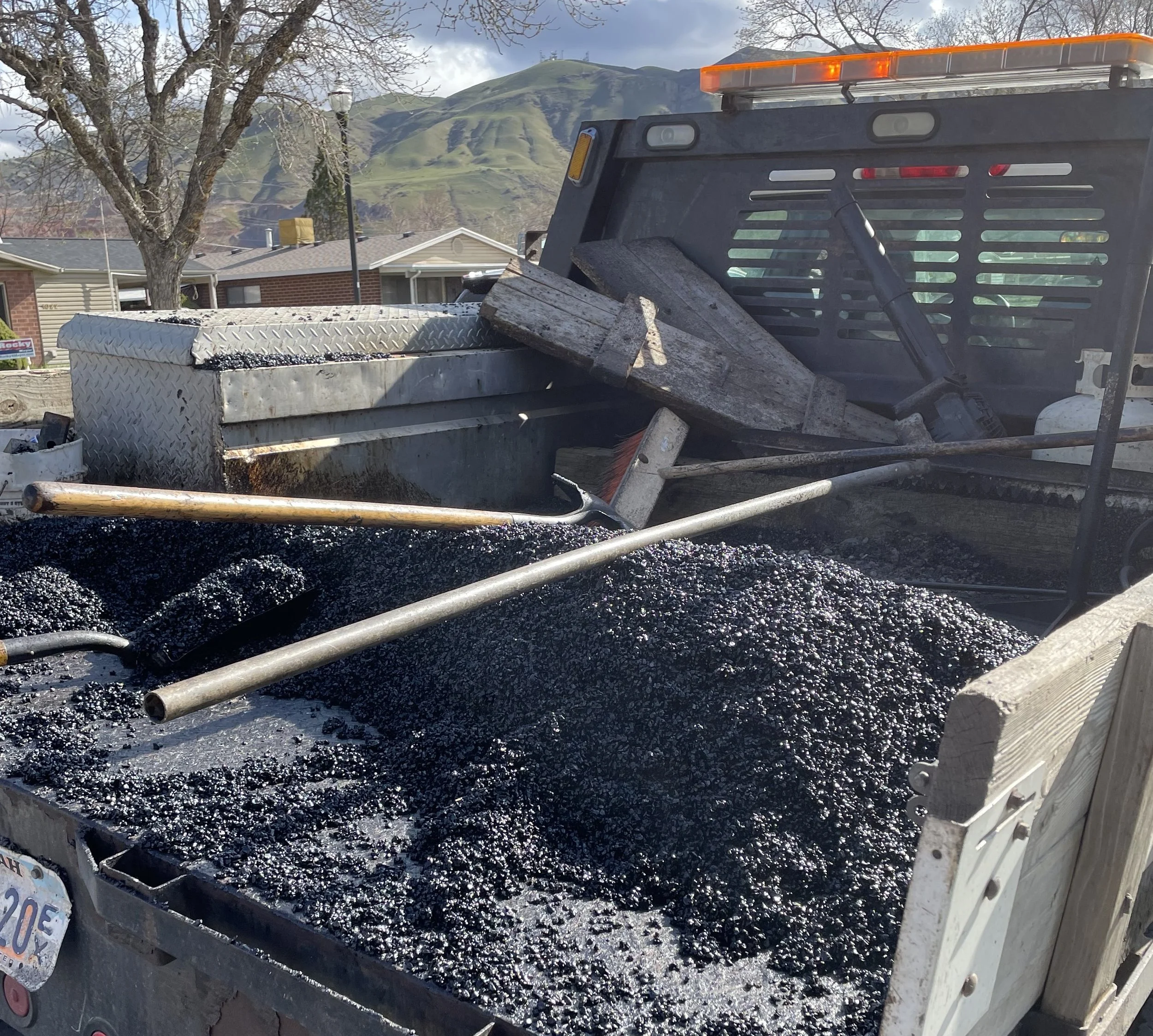 A work truck bed filled with mixed asphalt and hand tools.