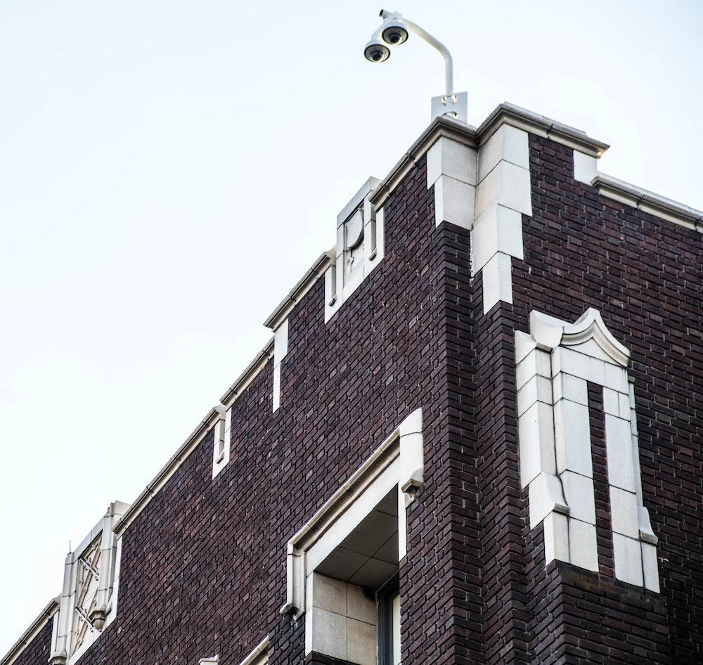 Looking up at corner of West High building to see modern lights on top.