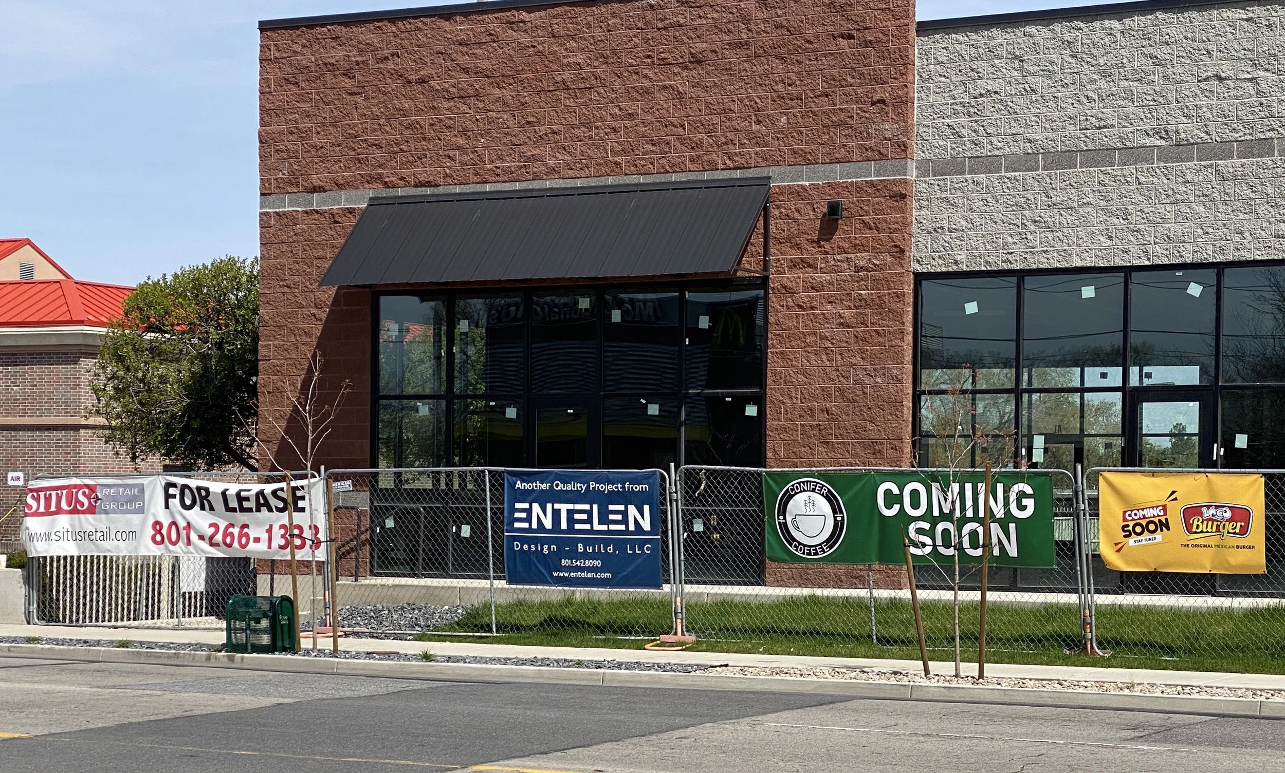 A fenced-off line of storefronts nearing complete. For Lease and Coming Soon signs on the fence.