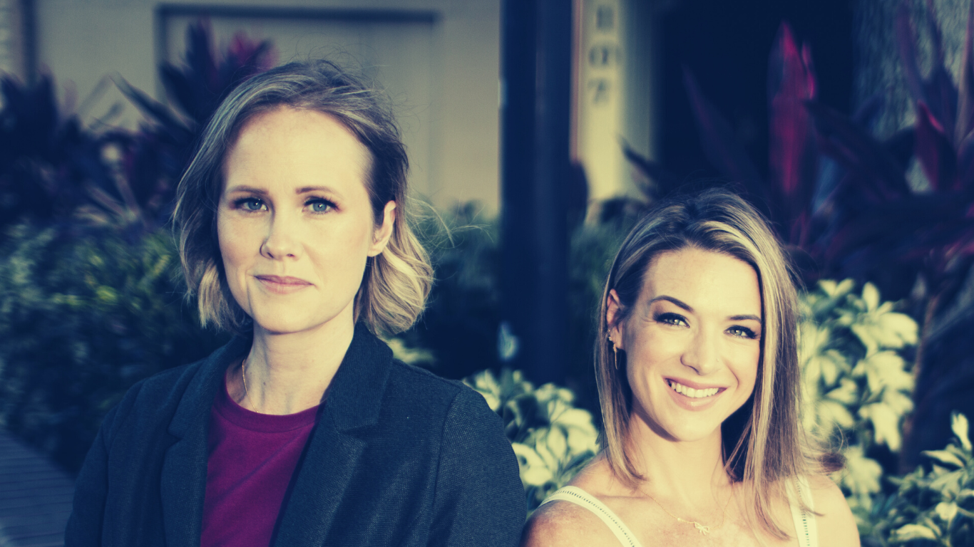 Melissa and Mandy, hosts of Moms and Mysteries Podcast sitting in front of a floral background.