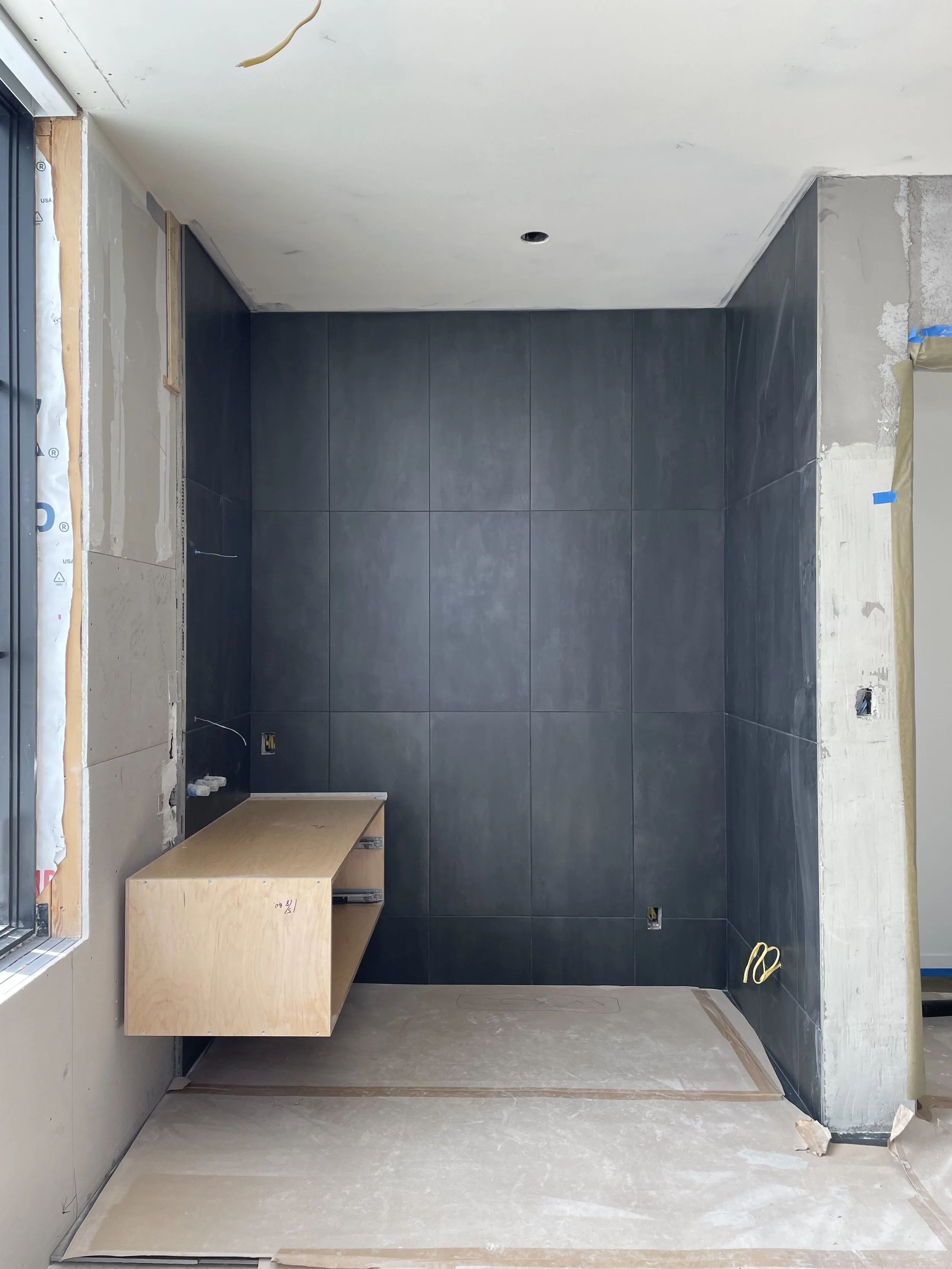 Partially constructed room with dark wall tiles, a wooden structure, and construction materials on the floor.