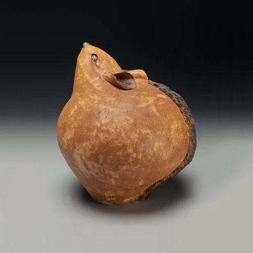 A brown pear-shaped sculpture of a mouse by Pam Brewer against a black and grey background