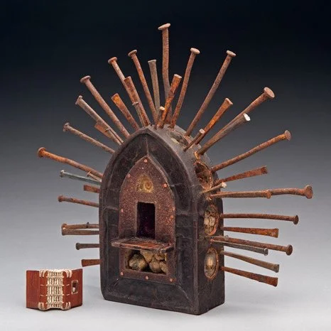 A pointed arch wooden sculpture by Daniel Essig with vintage nails sticking out from the top in all directions