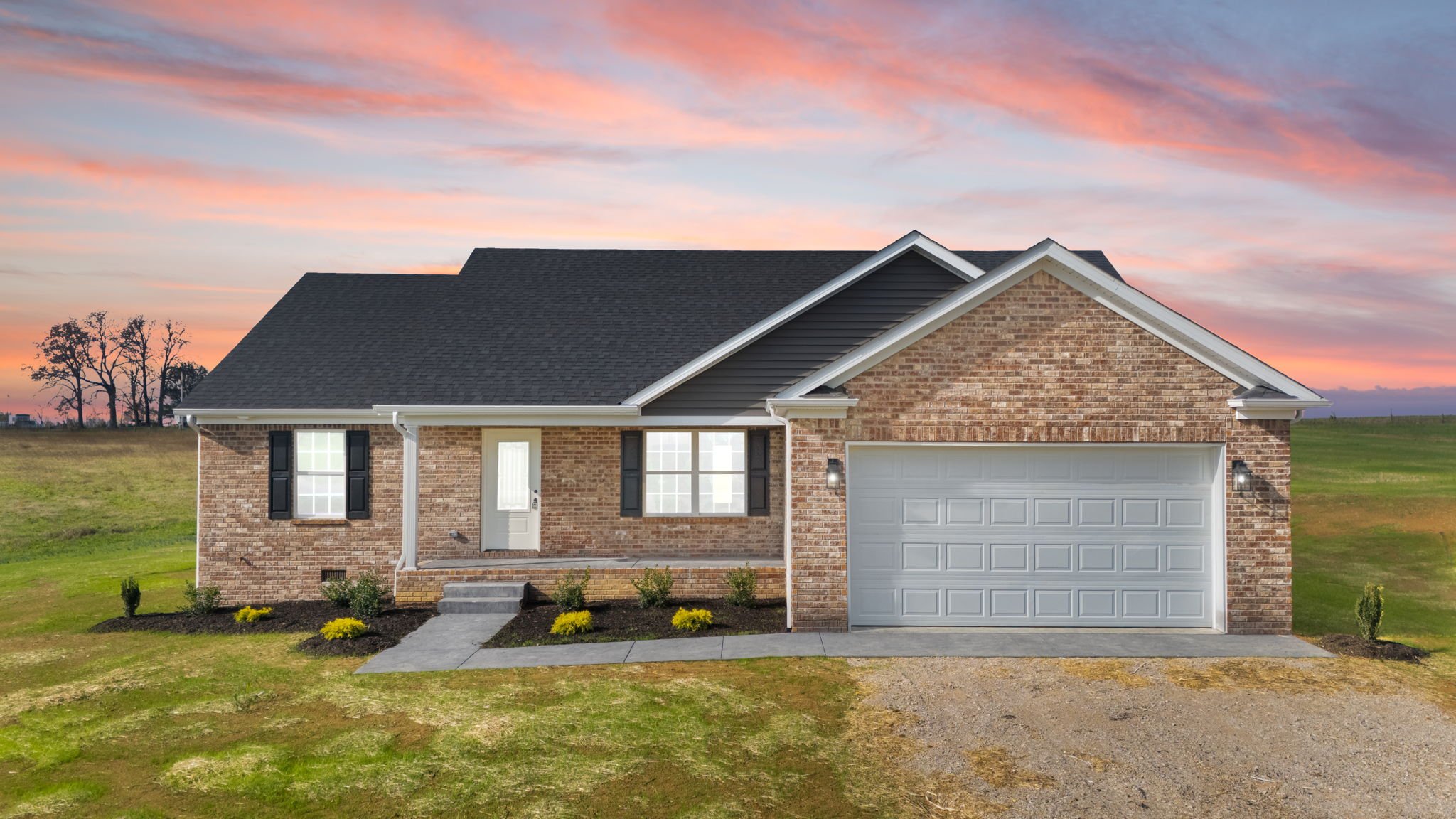 Brick house with black shutters, white garage door, and front porch with steps, set against a colorful sunset sky and green lawn.