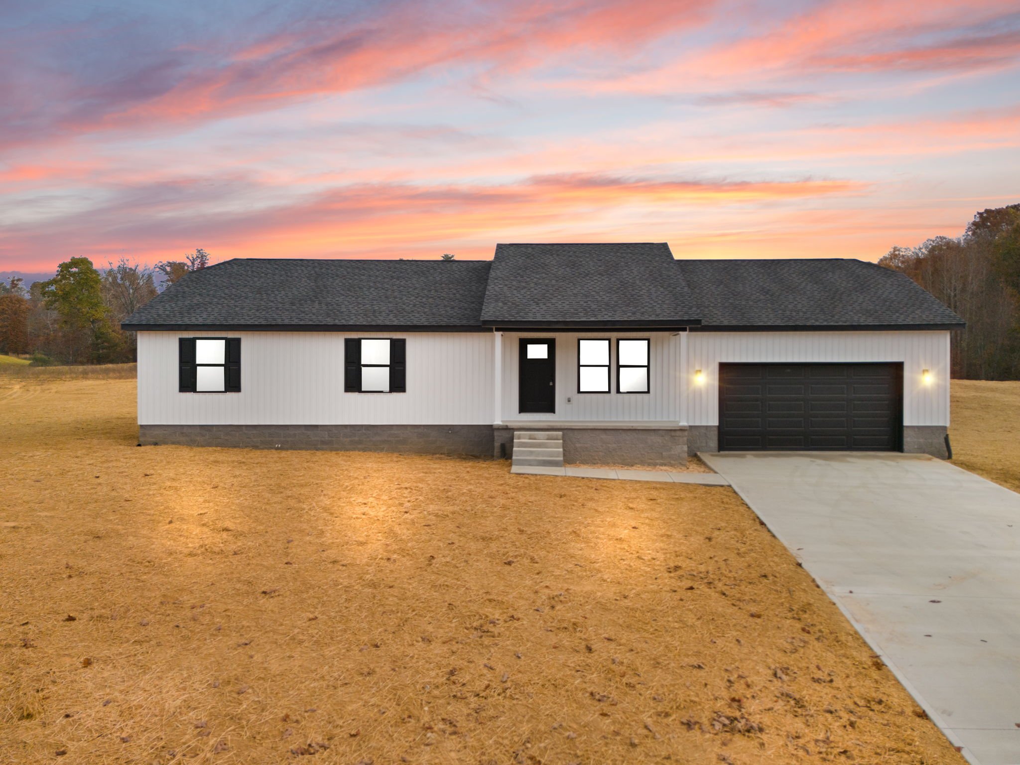 New white single-story house with black shutters, black front door, attached garage, and a driveway during sunset.