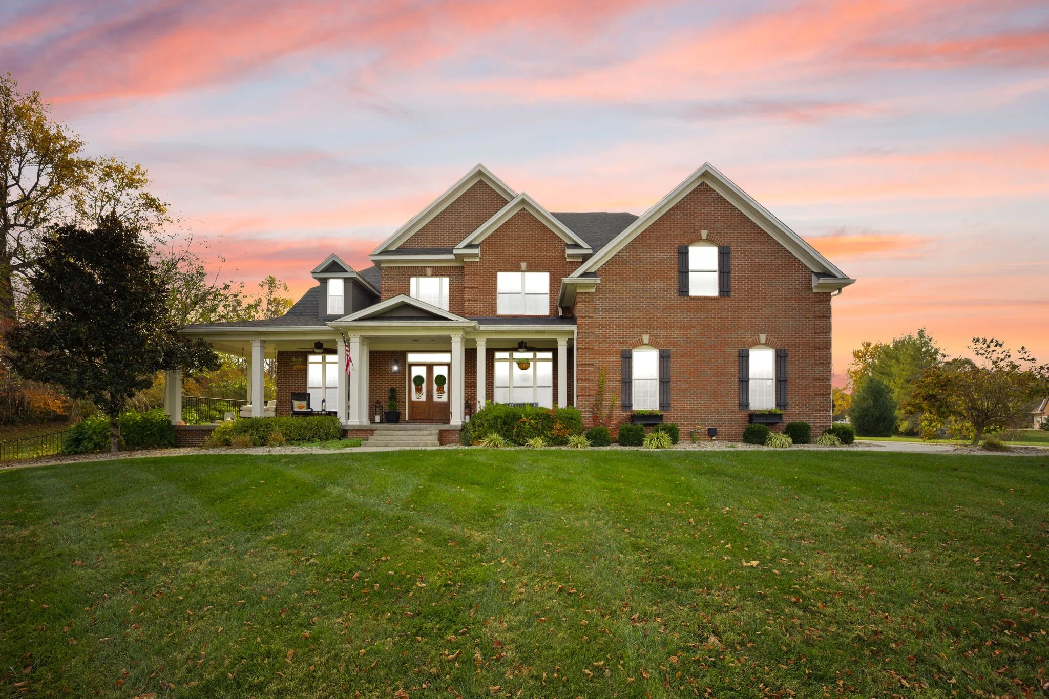 Large brick house with a well-maintained lawn and a sunset sky.