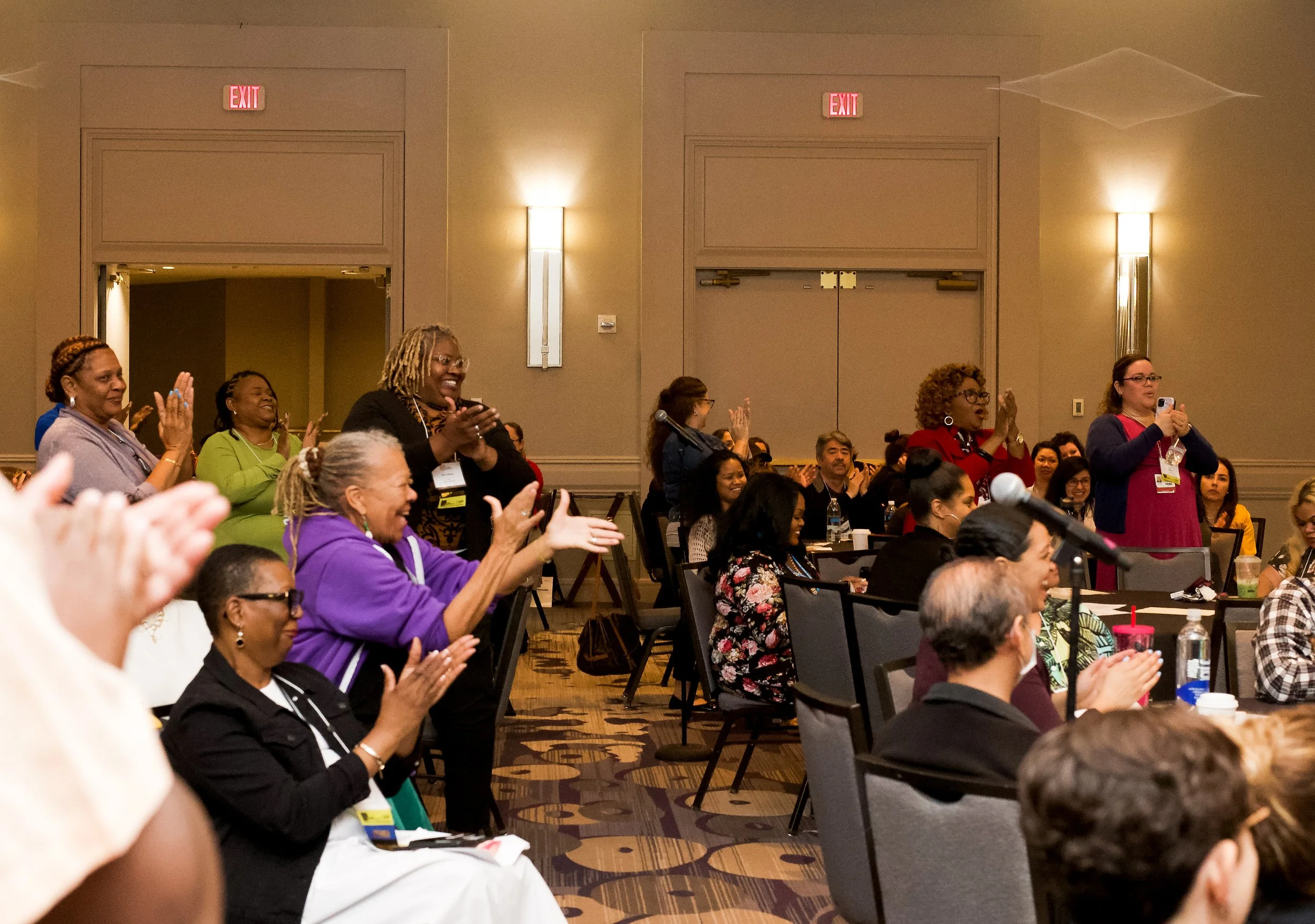 Group of women in a conference room standing, clapping, and taking photos during a presentation or event.