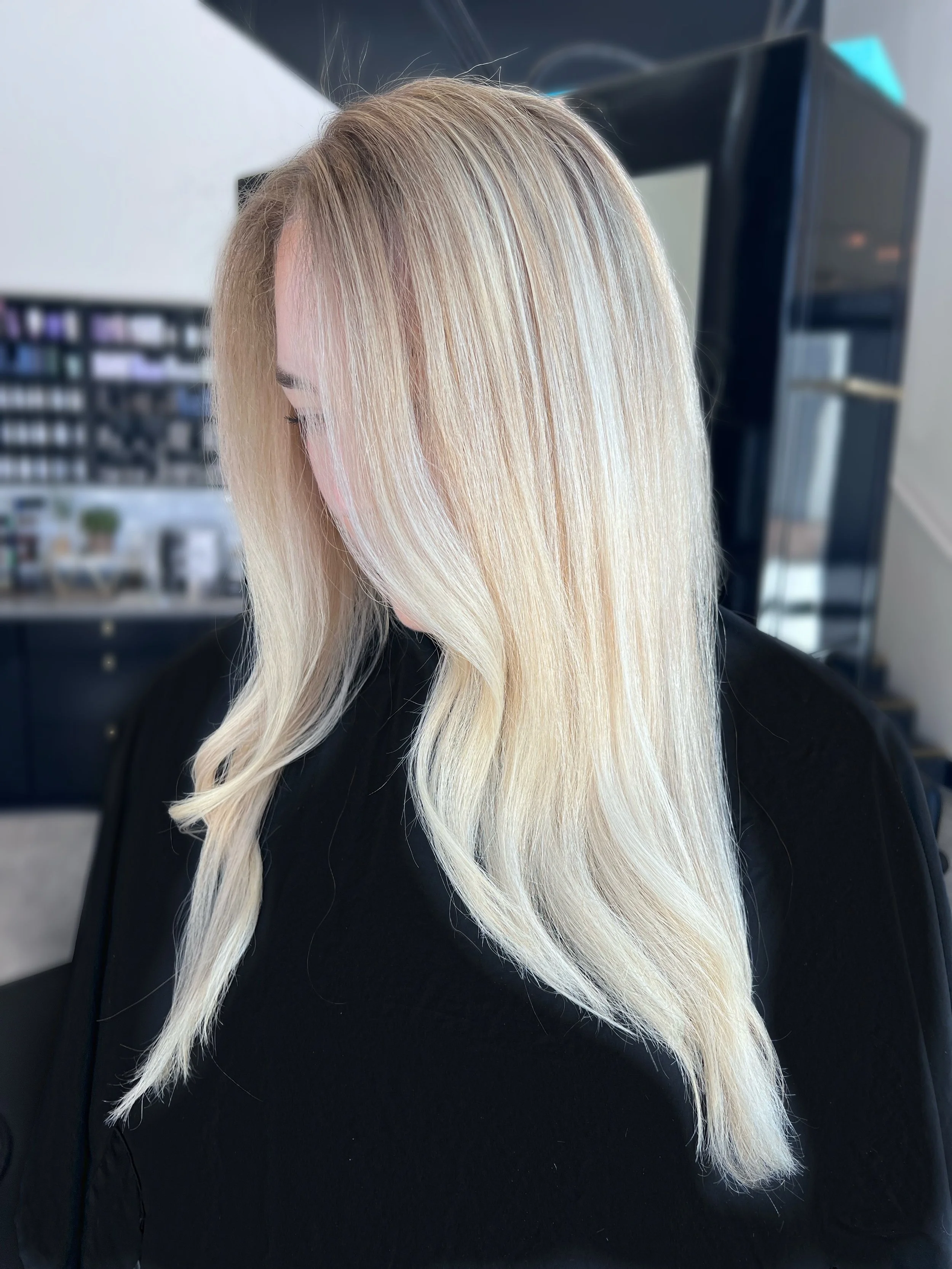 Person with long, wavy blonde hair wearing a black top inside a luxury salon setting.