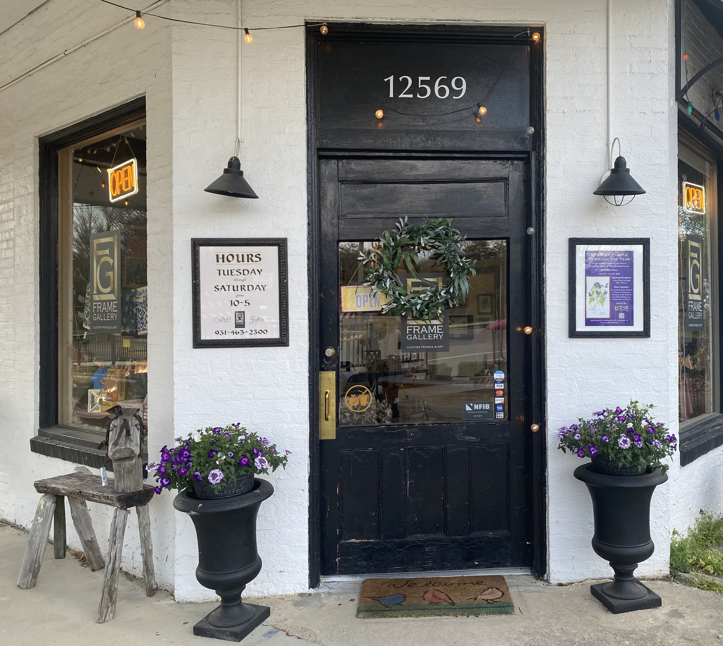 photograph of Frame Gallery Gifts & Art's entrance surrounded by purple potted flowers and a purple and green wreath on the door in sewanee, tennessee